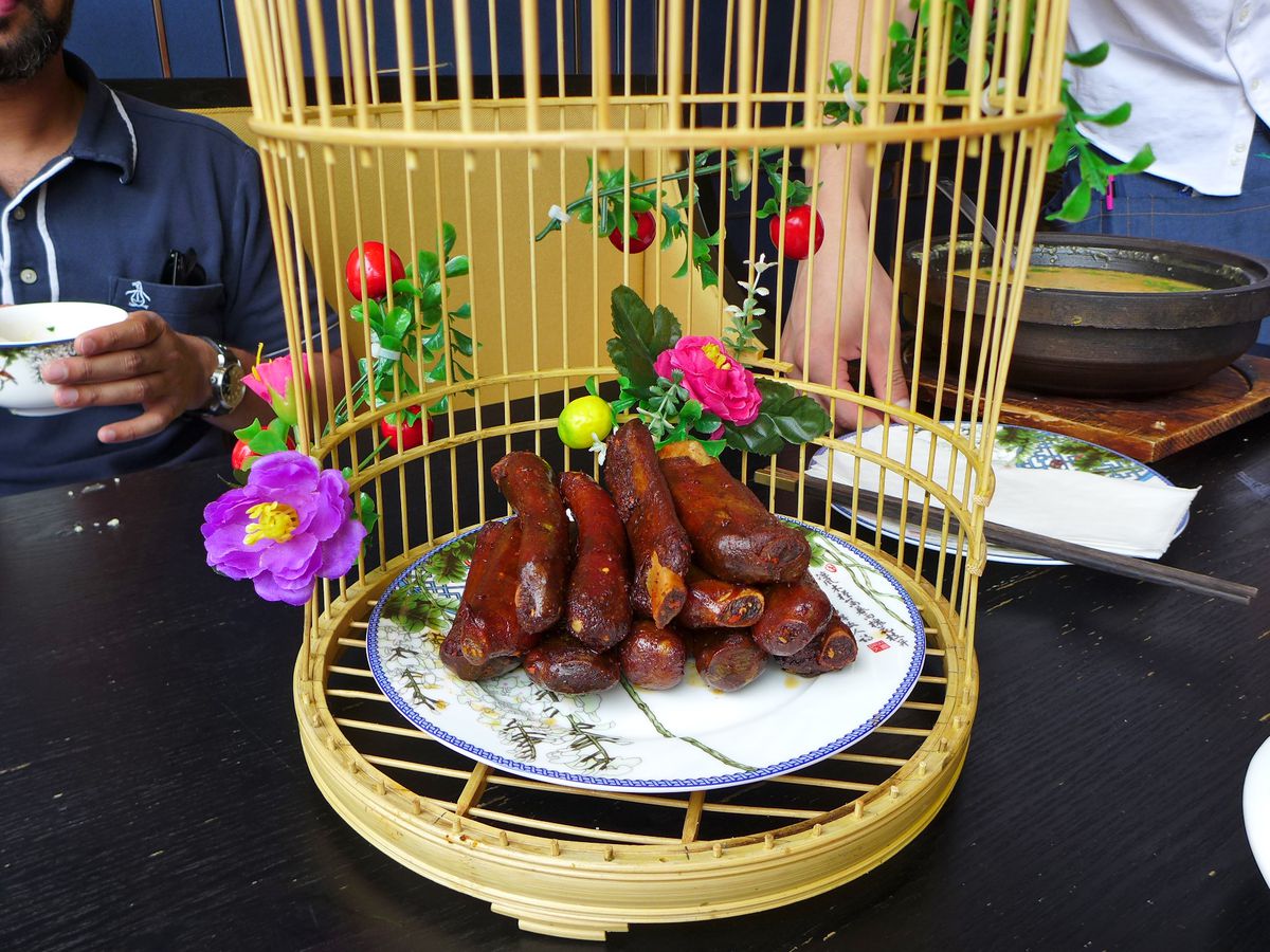 A bird cage twined with plastic flowers contains a pile of pork ribs.