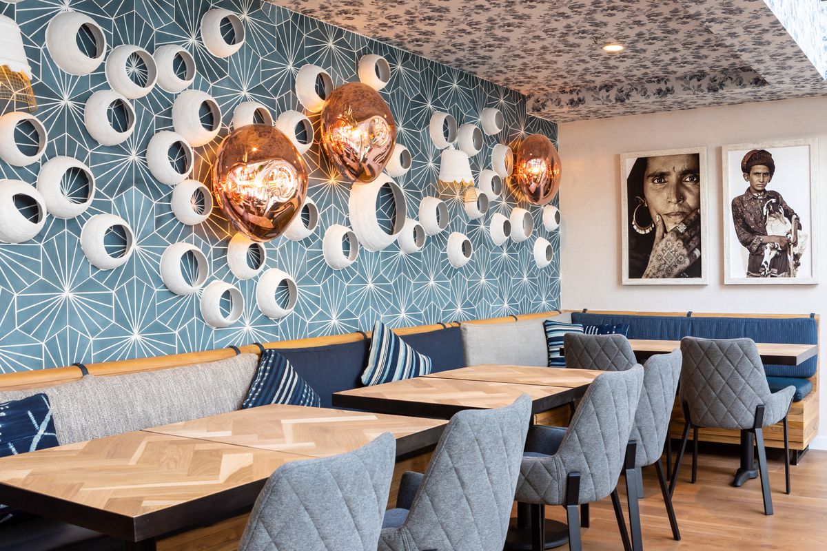 Wooden tables in front of geometric blue and white wallpaper and rounded art fixtures hung on the walls.