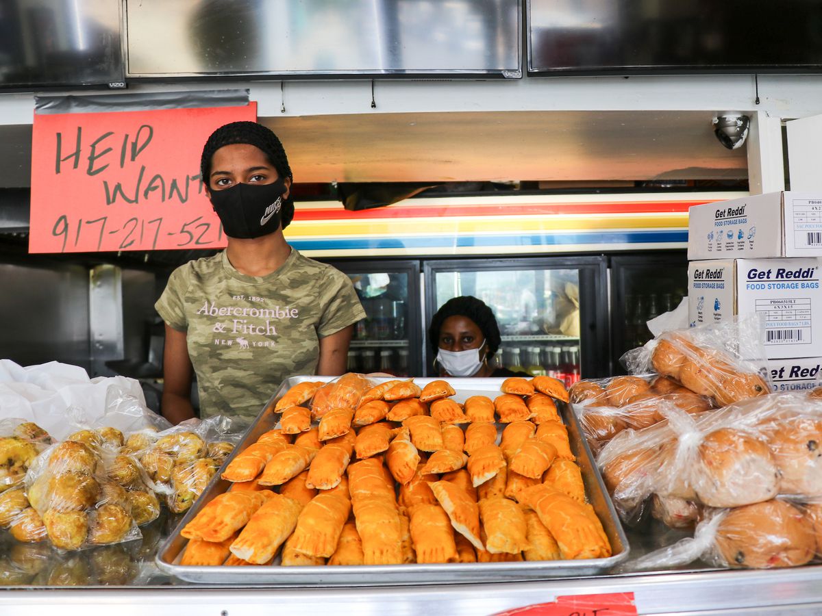 Two workers are behind the counter laid with Guyanese pastries like cheese rolls and bara.