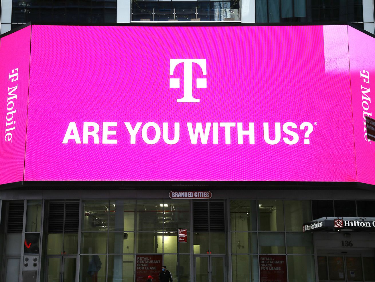 T-Mobile network advertisement seen on a Jumbotron in Times Square reads, “T-Mobile. Are you with us?”