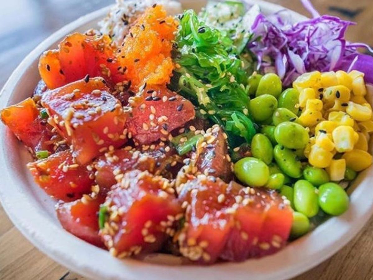 A poke bowl with diced red tuna, edamame green beans, yellow corn, and green leaves.