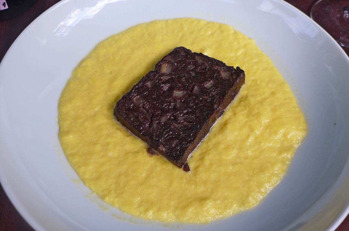 A bowl of yellow scrambled eggs with a rectangle of almost black blood sausage in the middle.
