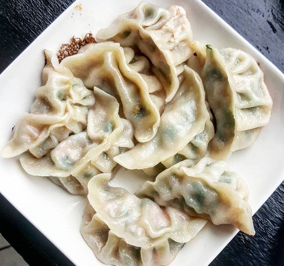 Overhead view of a square white plate covered with steamed, pleated dumplings
