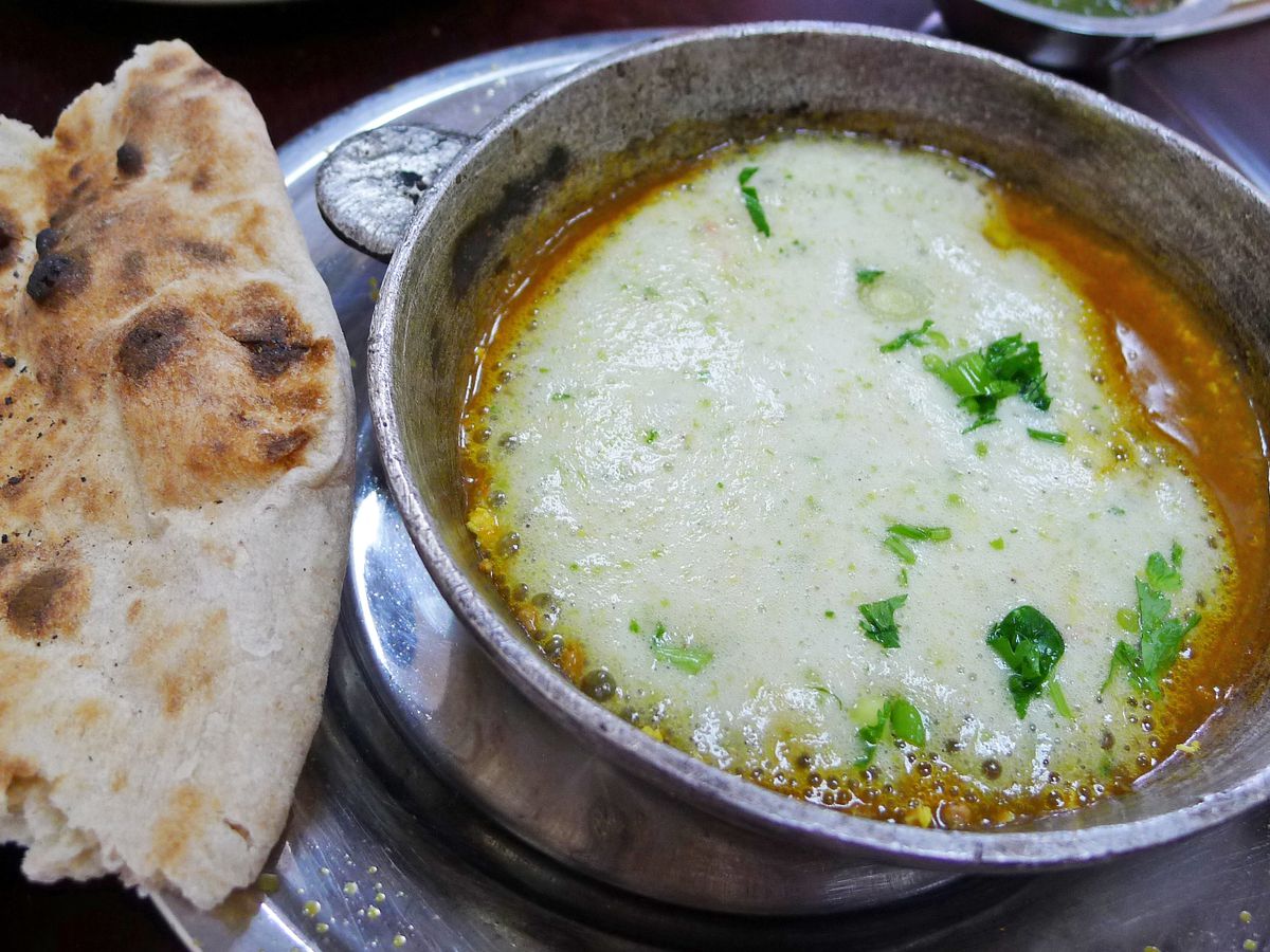 A metal pot with white foam on top and charred flatbread on the side.