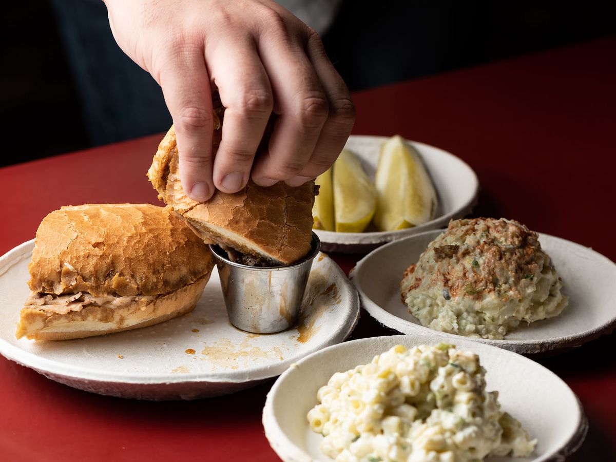 Philippe’s, a French dip restaurant, with red tables and a hand dipping a sandwich into jus.
