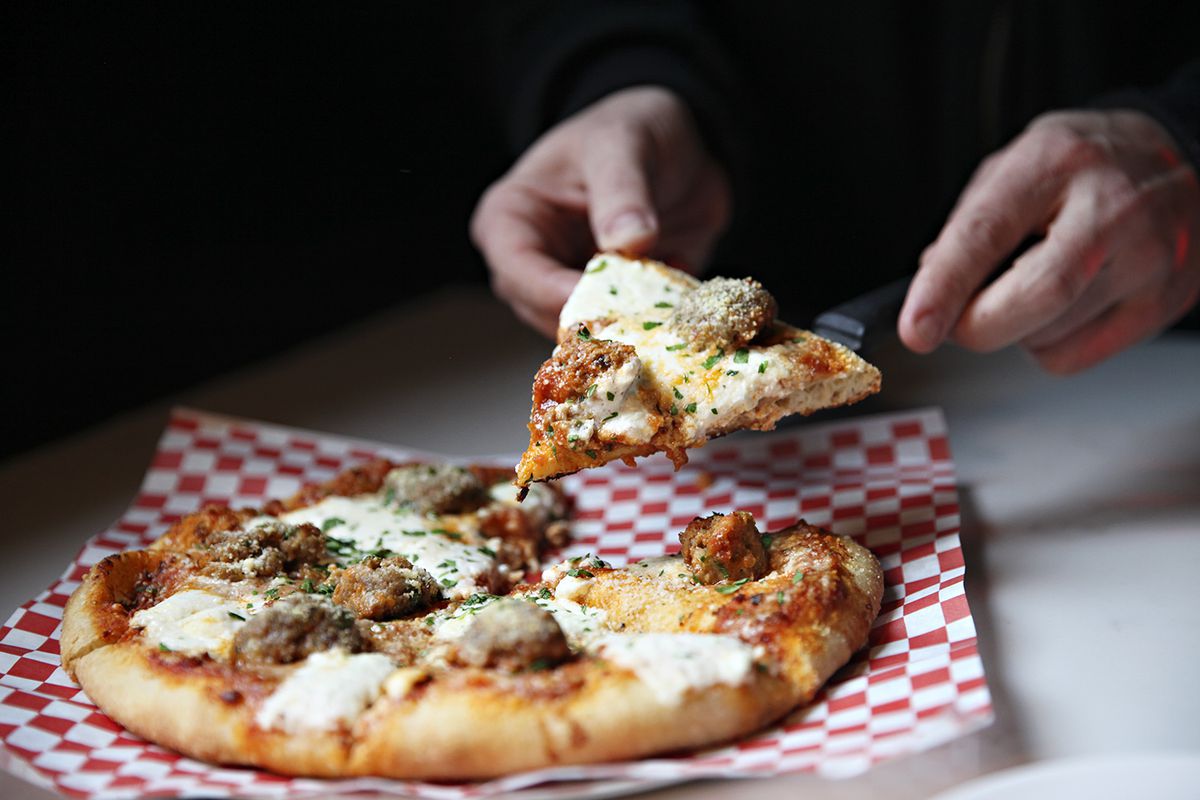 A hand reaches for a slice of Mucci’s sausage pizza