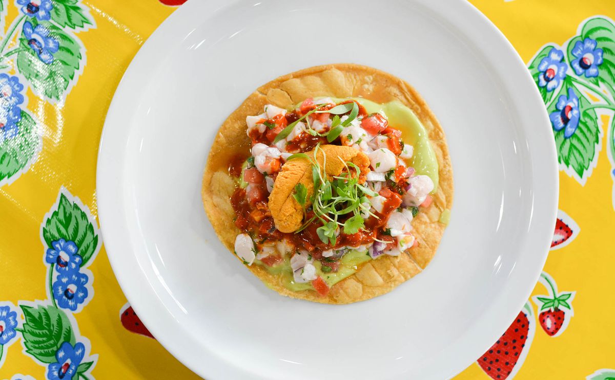 Colorful uni-topped ceviche tostada on a white plate with colorful tablecloth.