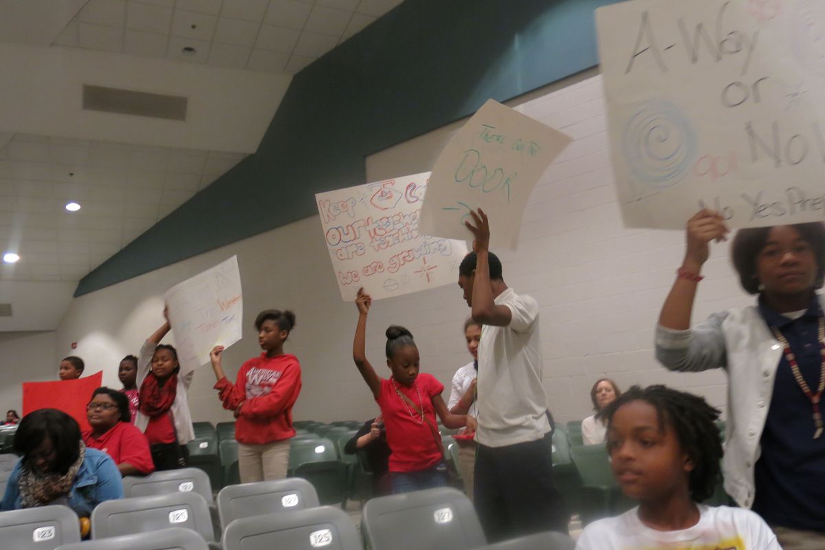 Several American Way students held signs during Monday night's school takeover community meeting with Yes Prep.
