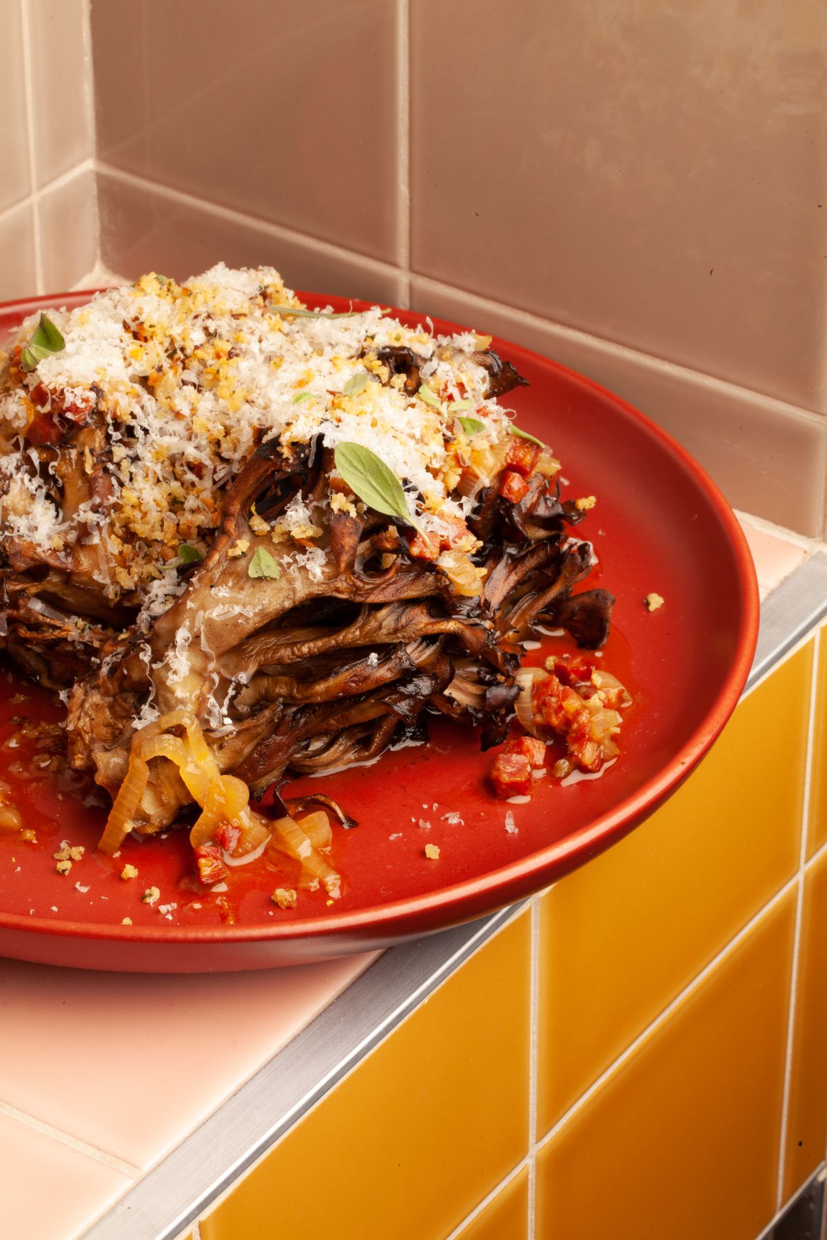 A red plate with large roasted mushroom pieces placed on top, covered in cheese and other garnishes.