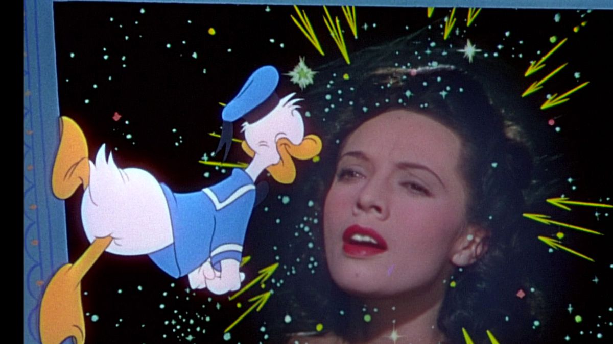 Donald Duck hangs off a vertical object with his feet while staring devotedly at singer Dora Luz, whose face hangs in the starlit sky in The Three Caballeros