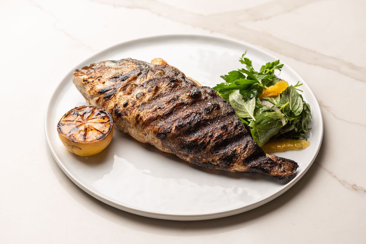 A whole fish fried atop a grill with skin on, shown at a new restaurant under a bright light.