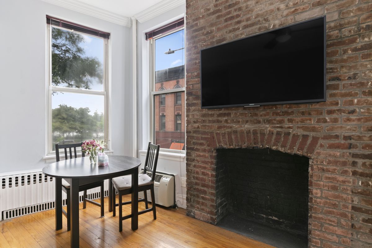 A living area with a small table, a decorative fireplace, a TV on the wall, and exposed brick.