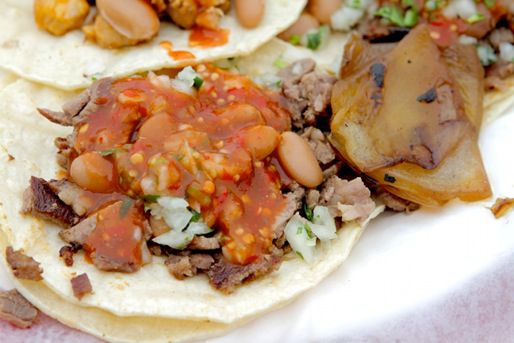 A close up photo of tacos with beans and meat on flour tortillas.