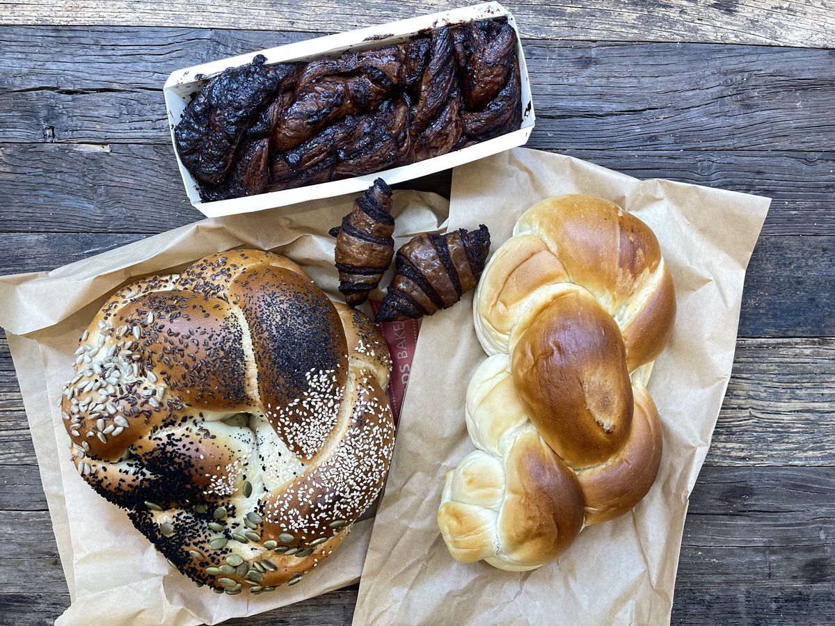 A spread of pastries and bread laid out above their brown wax sleeves on a wooden surface.