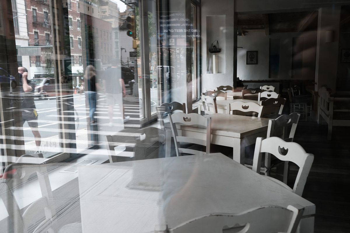 A row of white chairs and tables in an empty restaurant are facing a window looking out into a Manhattan street.