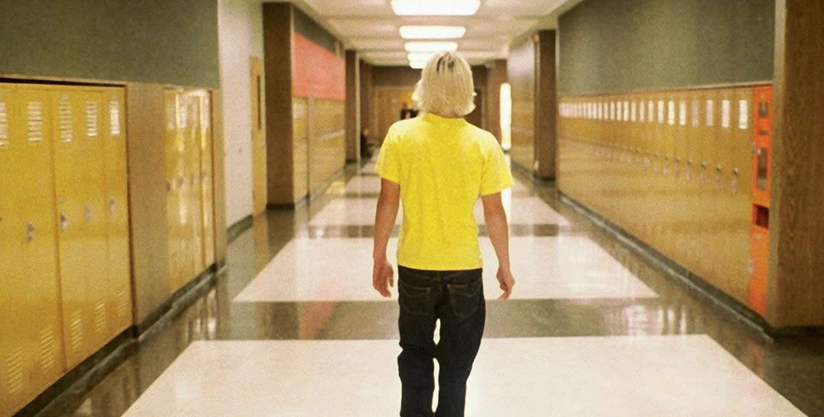 A teenaged boy walks down a school hallway.