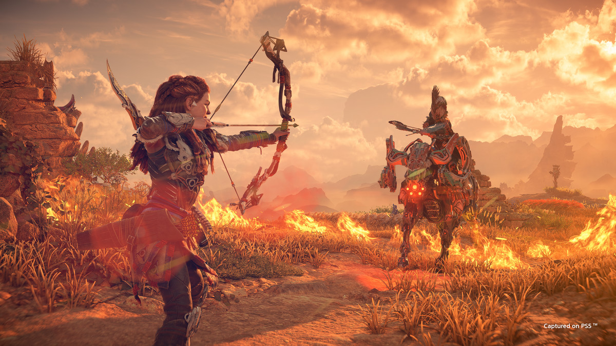 Aloy with her bow and arrow pulled back, aiming at a Tenakth warrior riding a Charger, in Horizon Forbidden West