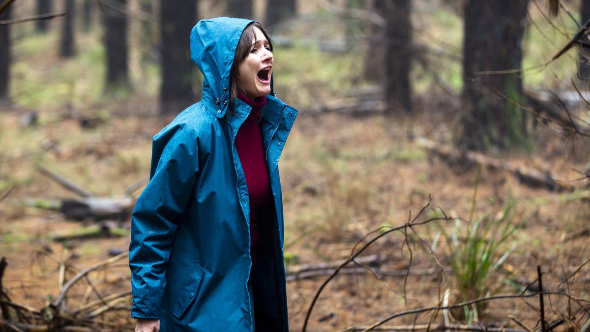 Emily Mortimer in Relic stands in the woods in a bright blue jacket, screaming.