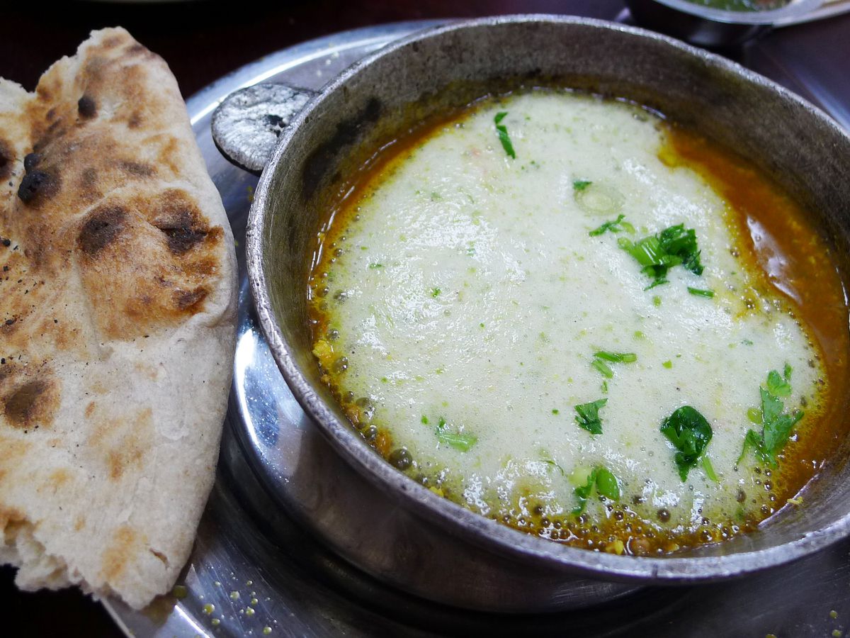 A bubbling pot of foamy brown good with a charred flatbread on the side. 