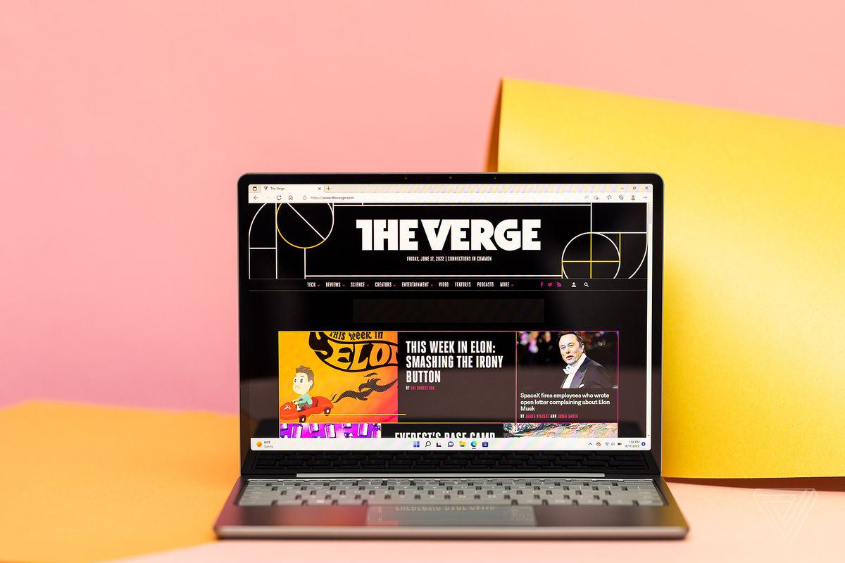 A sage-colored Microsoft Surface Laptop Go 2 with its screen open and facing the viewer in front of a pink and yellow backdrop.
