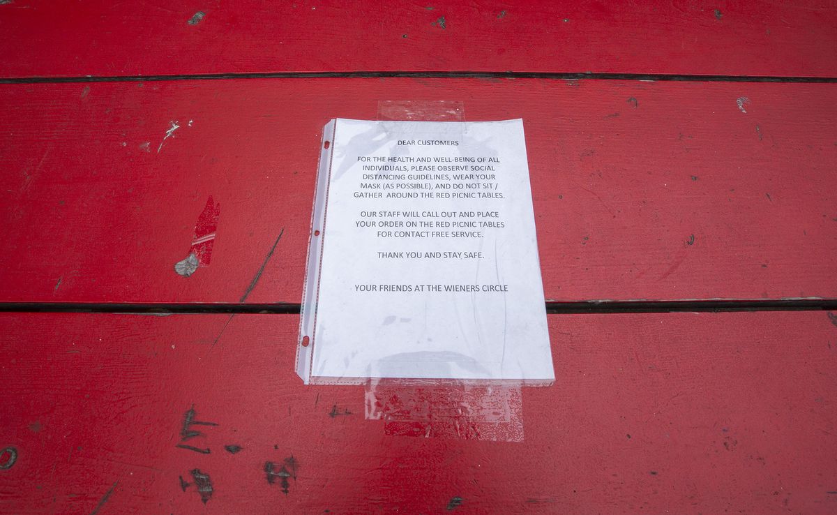 A paper sign in a plastic sleeve taped to a red wooden bench.