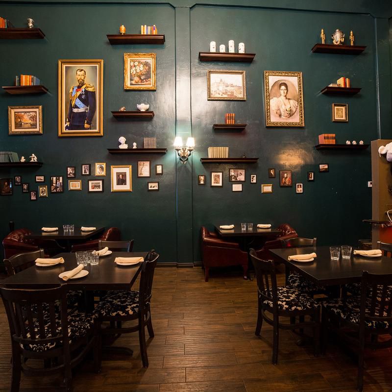 The interior of a dining room, with hunter green walls, old style portraits covering the walls and dark dining tables and chairs.