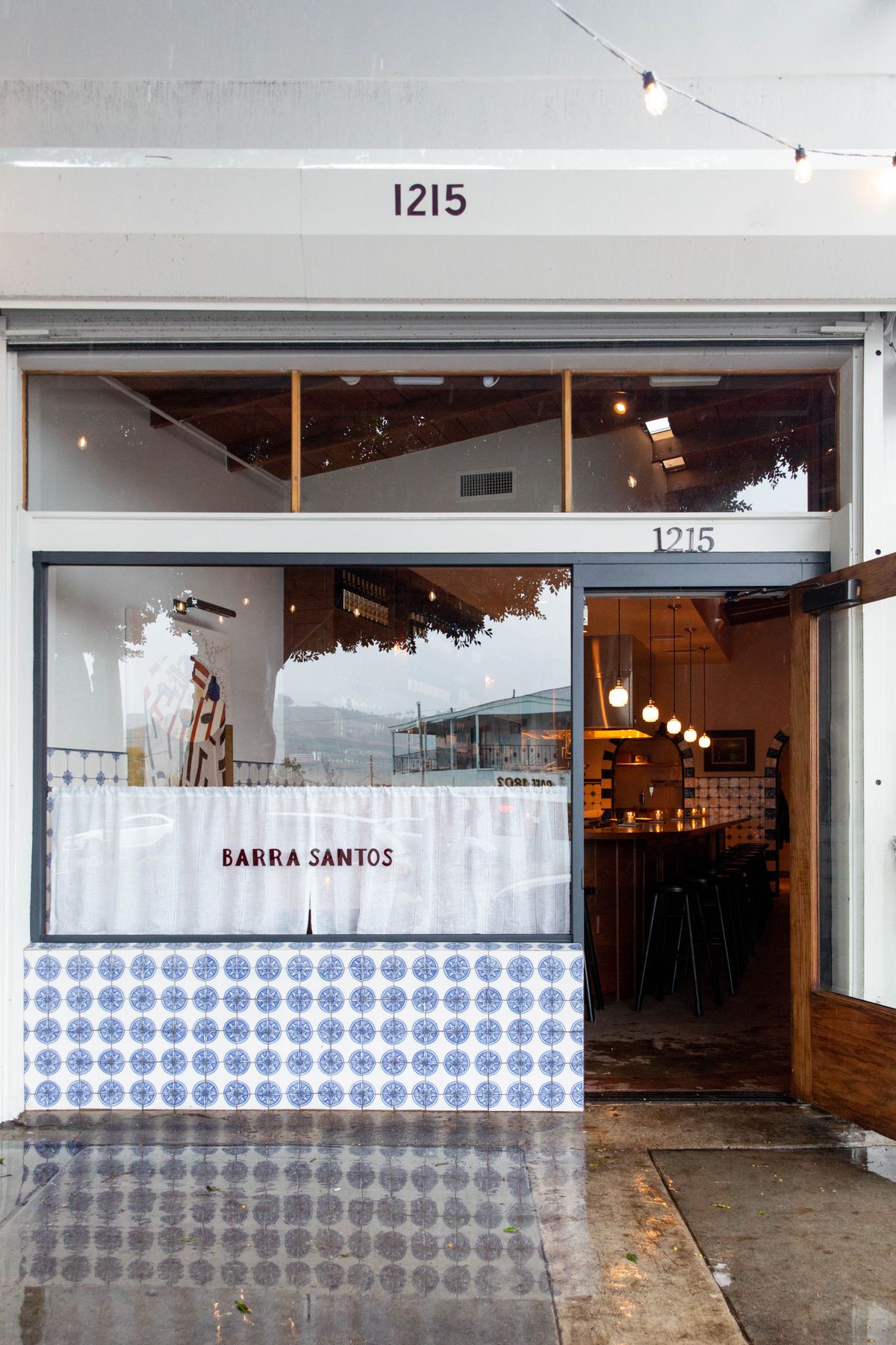 The exterior of a rainy new restaurant space with white curtains.