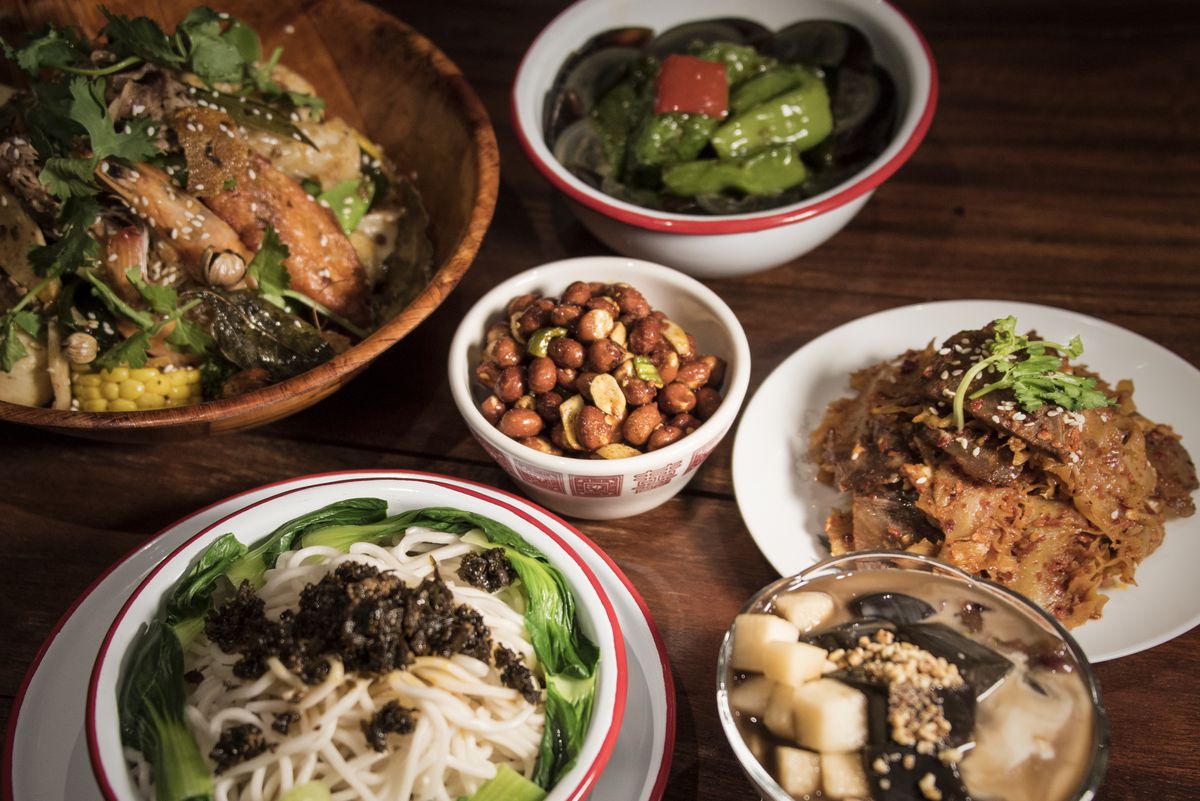 A spread of dishes at MáLà Project, including dan dan noodles, shelled peanuts in a cup, and dry pot in a wooden bowl