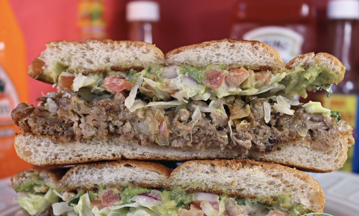 Closeup cross-section of a Mexican torta, with meat, guacamole, and more sandwiched between bread