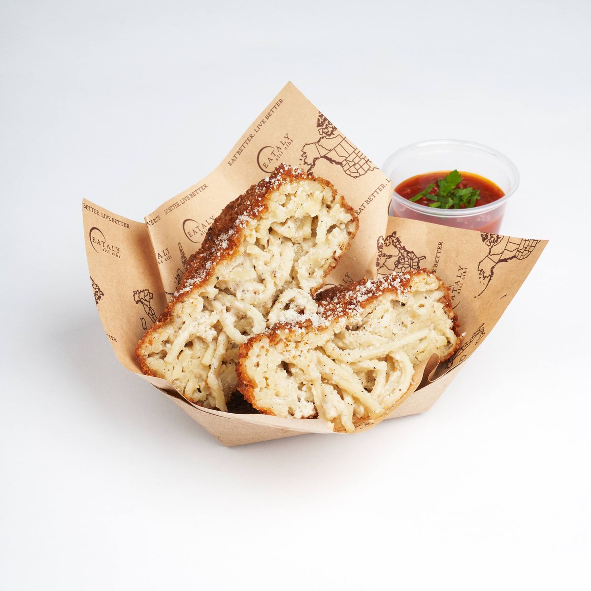 A cardboard boat holds fried and breaded cacio e pepe. Behind it to the right is a plastic container of tomato dipping sauce.