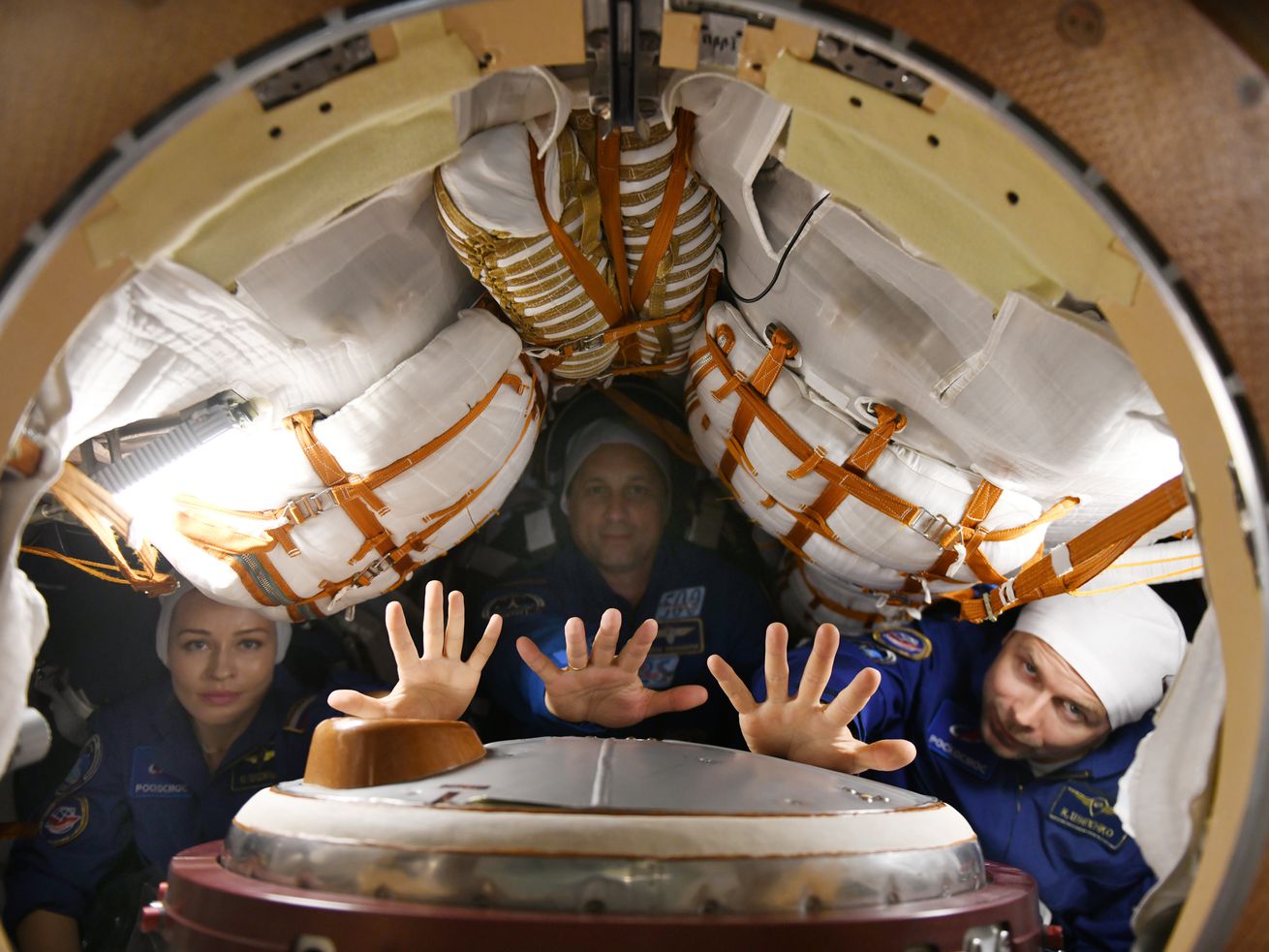 Russian cosmonauts are shown reaching toward the camera, framed in a circular doorway, with equipment surrounding them.