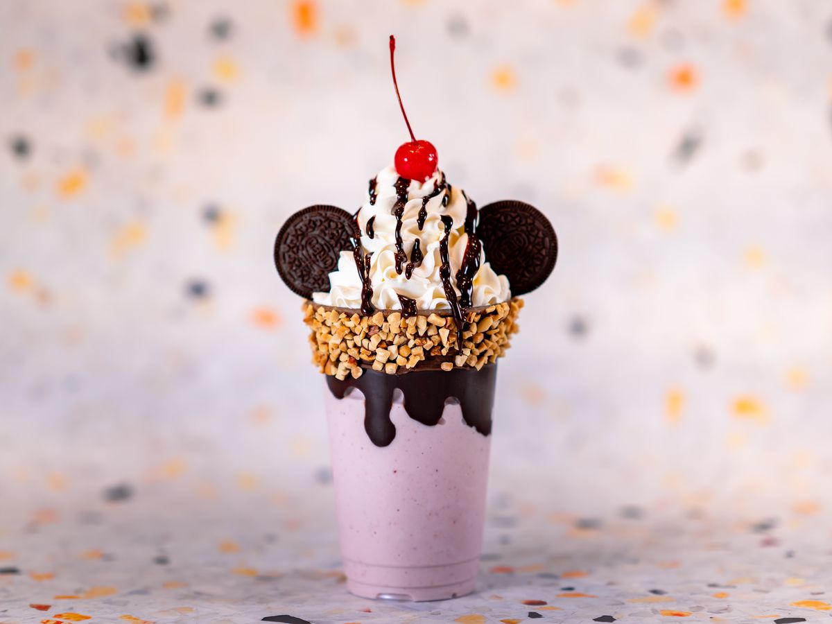 A milkshake topped with whipped cream, a cherry, and cookies that look like mouse ears.