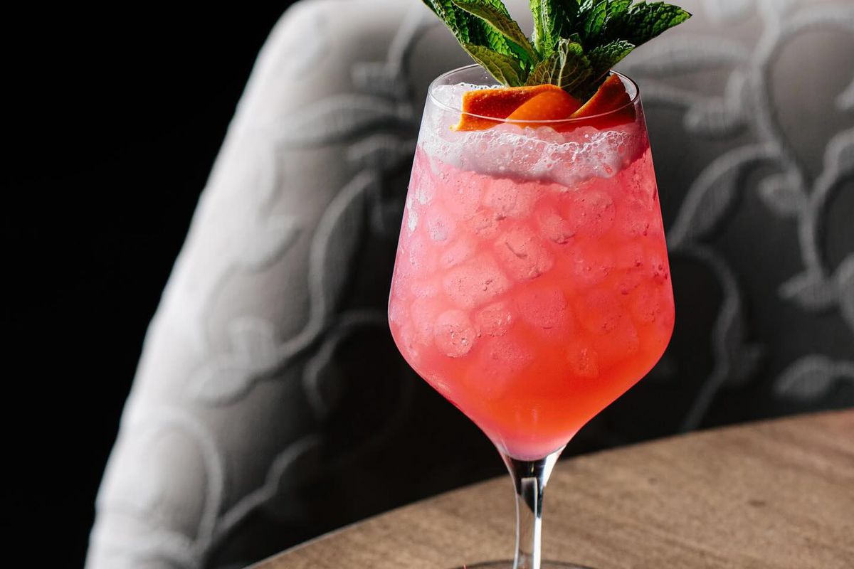 A pink cocktail filled with ice with a berry and mint garnish.