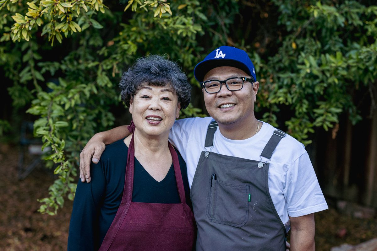 A mother and son standing next to each other wearing aprons and the son wearing a blue baseball cap.