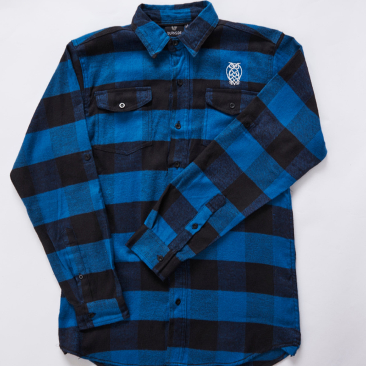 A blue and black flannel shirt with a small owl logo embroidered near the left shoulder