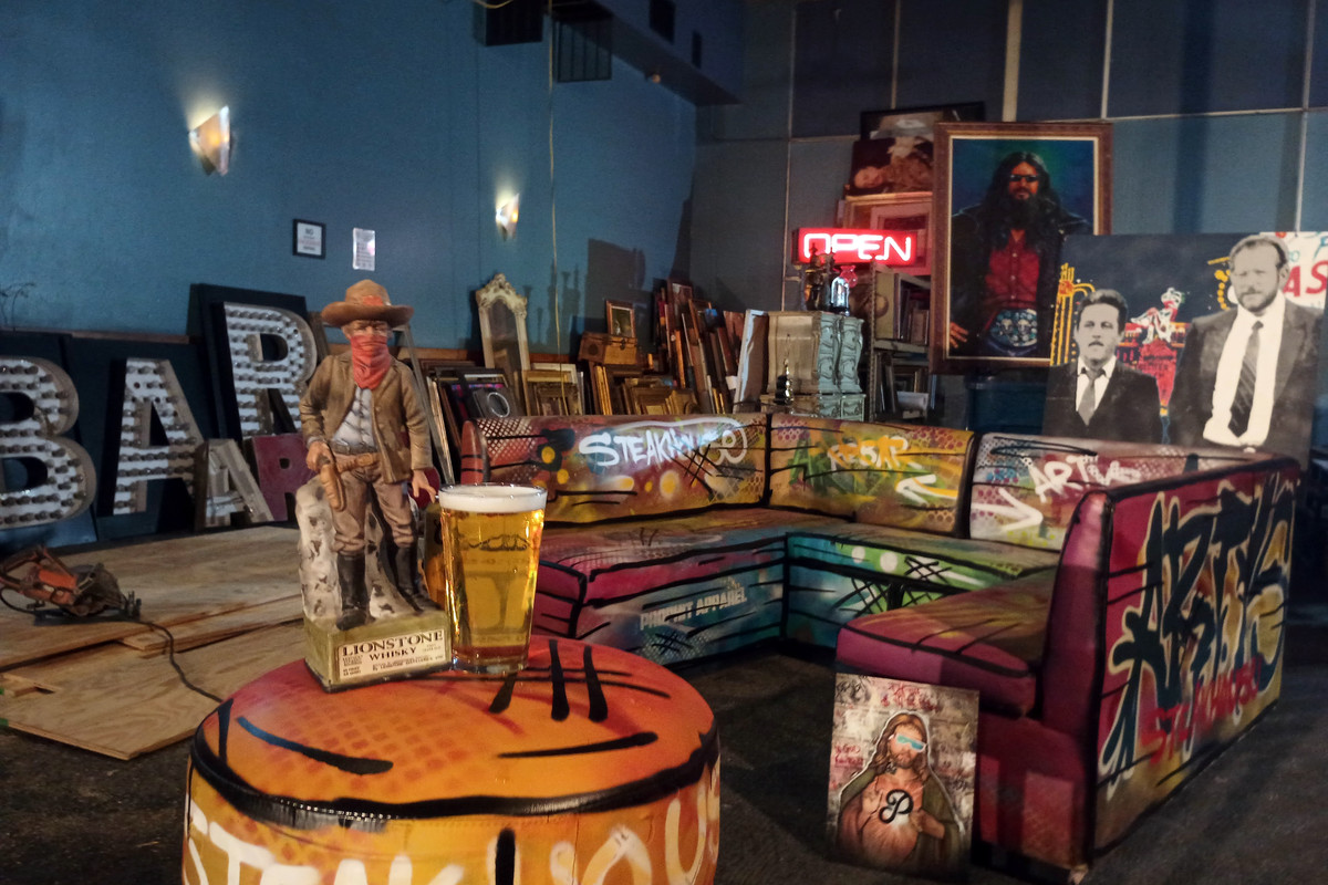 A colorful collection of various works of art including a spray painted couch, a cowboy statue, and frames sitting along a light blue wall.