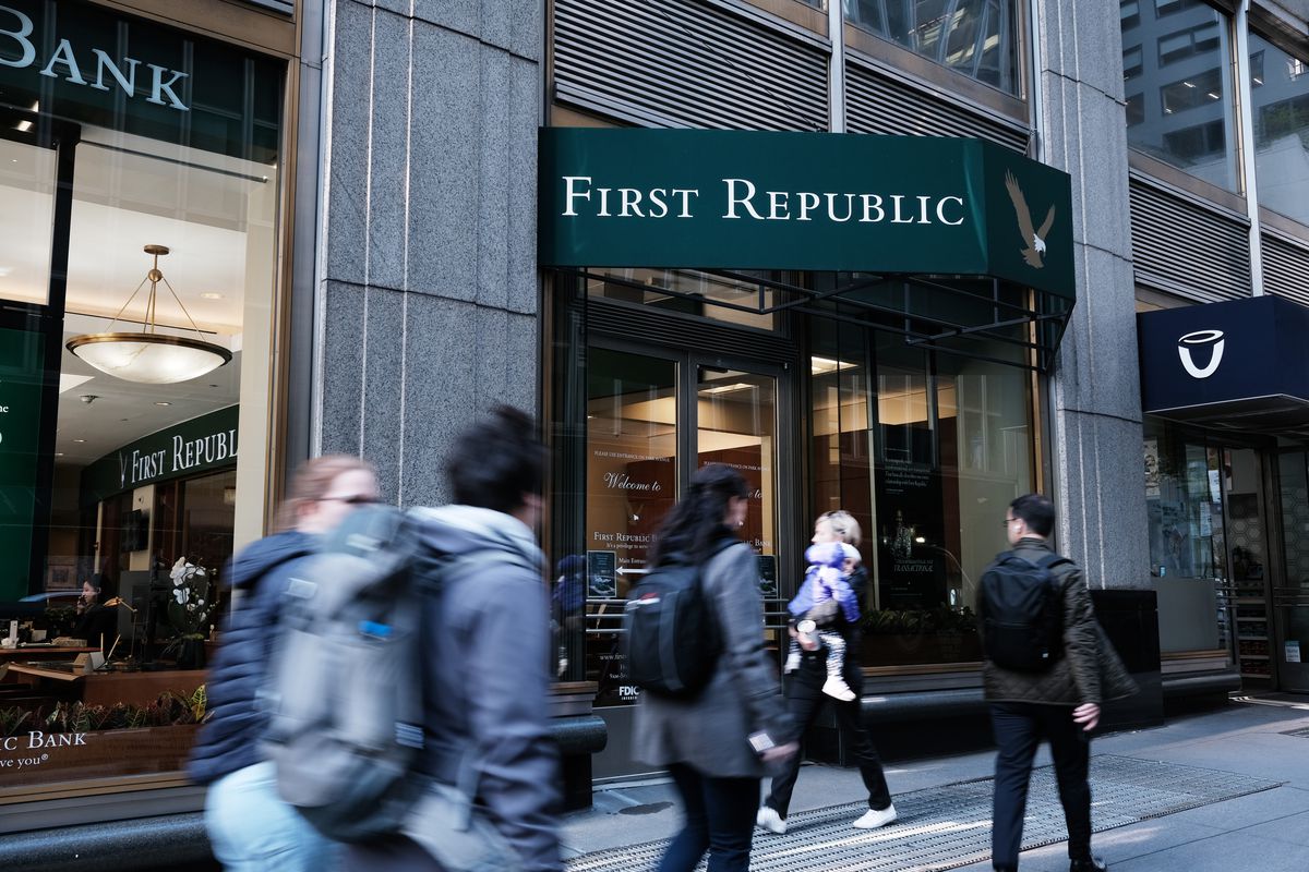 People walk past the entrance to First Republic Bank, a stone building with large windows and a green awning.