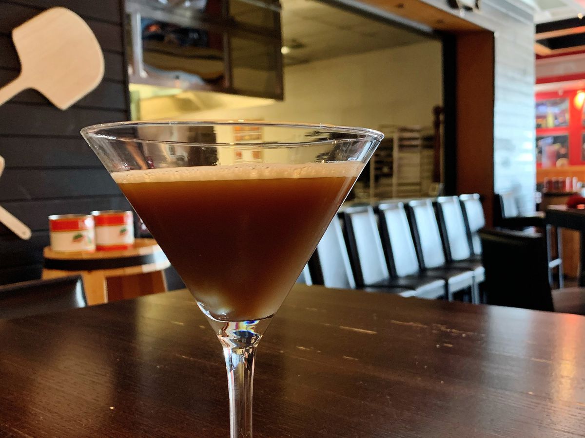 A dark brown espresso martini in a martini glass on a table in Kenny’s East Coast Pizza.