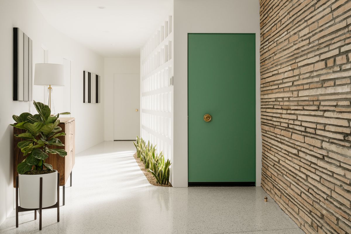The home’s entryway has a green door, plants, and a stone wall. 