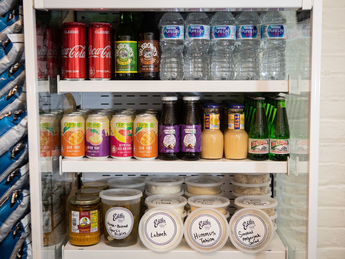 Bottles of water, cans of soda, and plastic containers of pre-made dips and spreads line three shelves a small refrigerator