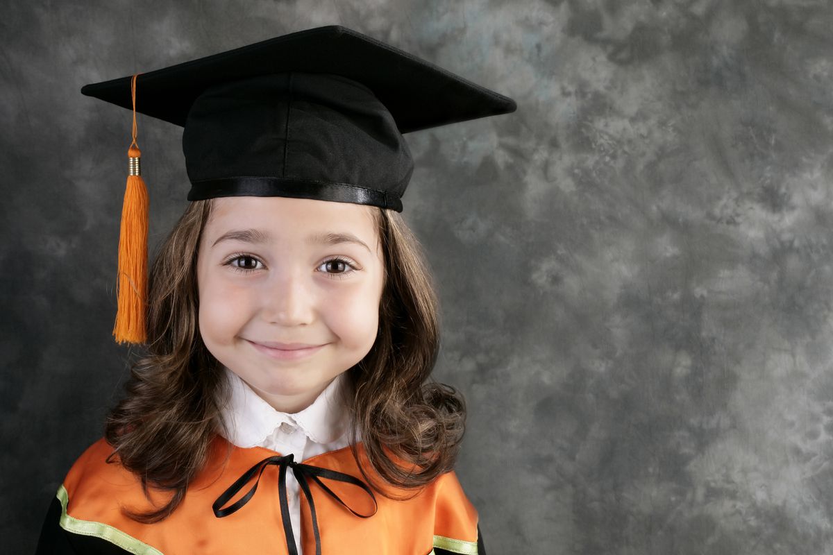 An elementary school child wearing a mortarboard and smiling for her portrait.
