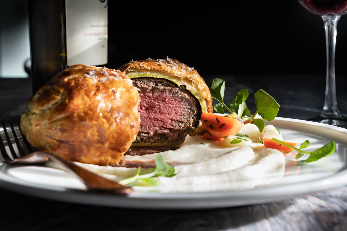 A round white plate contains a beef Wellington cut in half. 