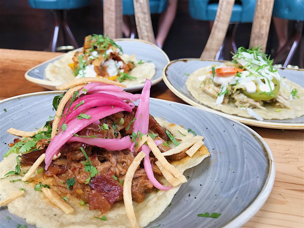 Close up of a taco topped with pickled onions; two plates with tacos in the background