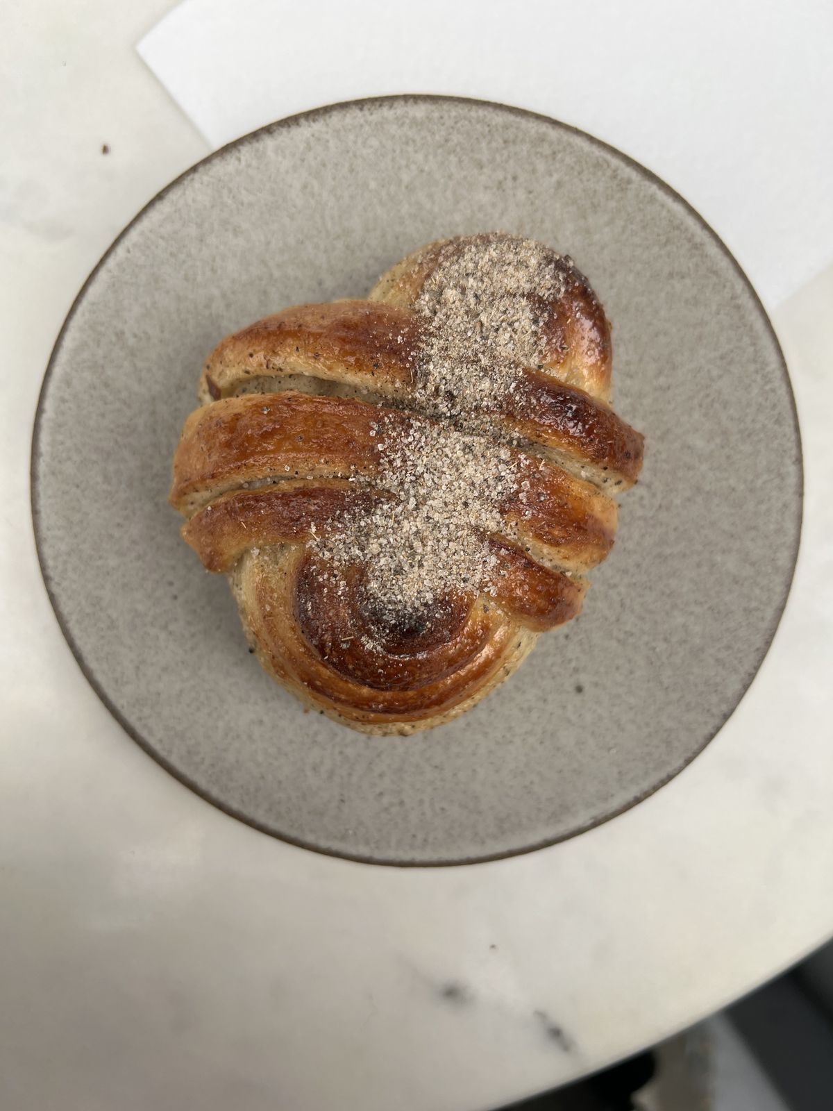 An overhead shot of the oven-burnished cardamom bun, sprinkled with sugar, sitting on a grey plate.