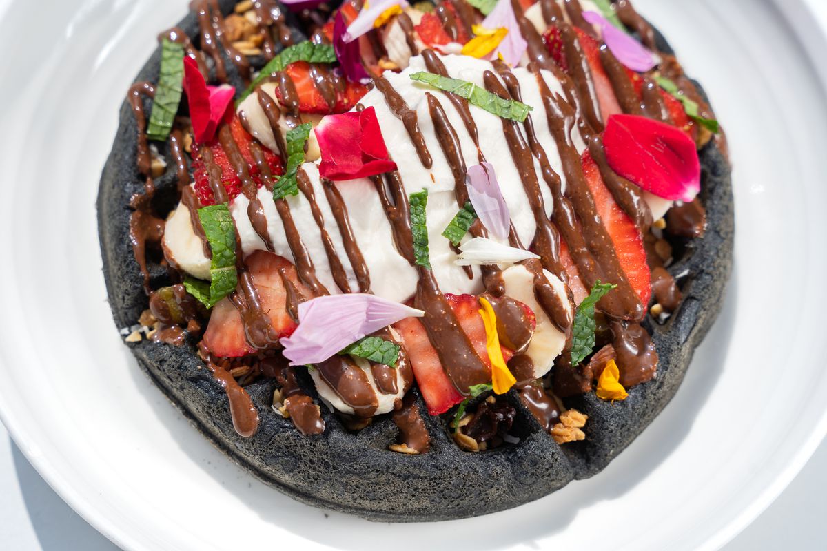 An overhead shot of a black waffle with cut fruit and drizzles of chocolate at new LA restaurant Parakeet Cafe.