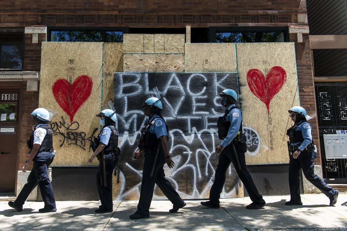 Chicago police officers walk by a boarded-up business Saturday during a massive peaceful protest in Chicago calling for police reform. 
