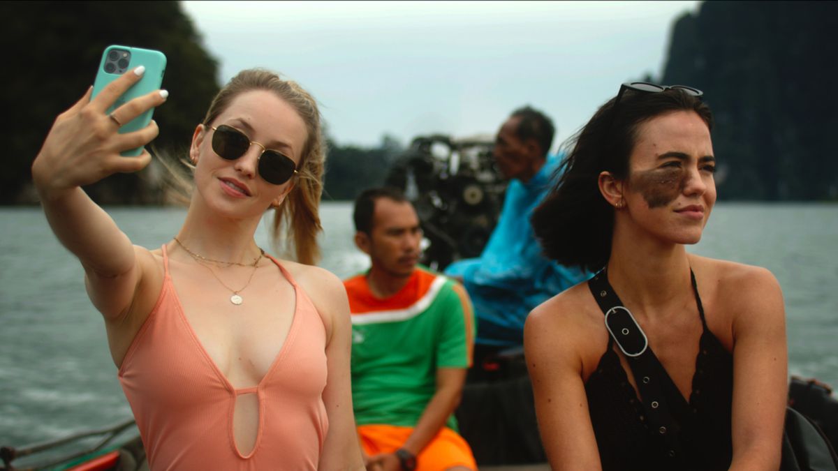 (LR) Emily Tennant takes a selfie next to Cassandra Naud in front of a motorboat in Influencer.