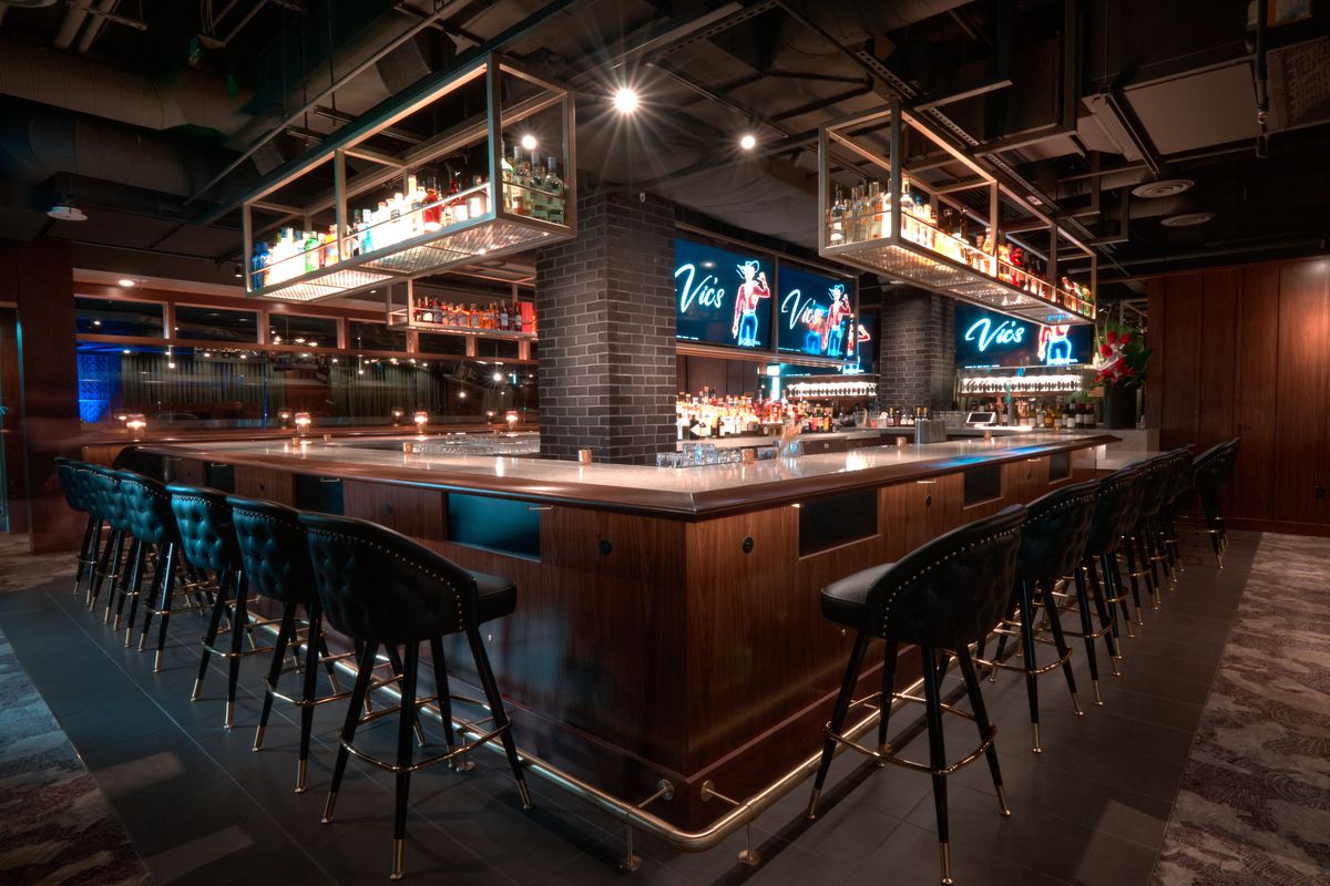 A bar surrounded by barstools, with TVs at the center.