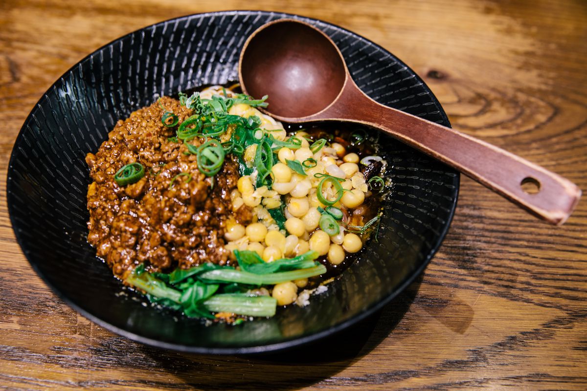 A bowl with minced pork, corn, scallions, and noodles; a brown wooden spoon sits on top.