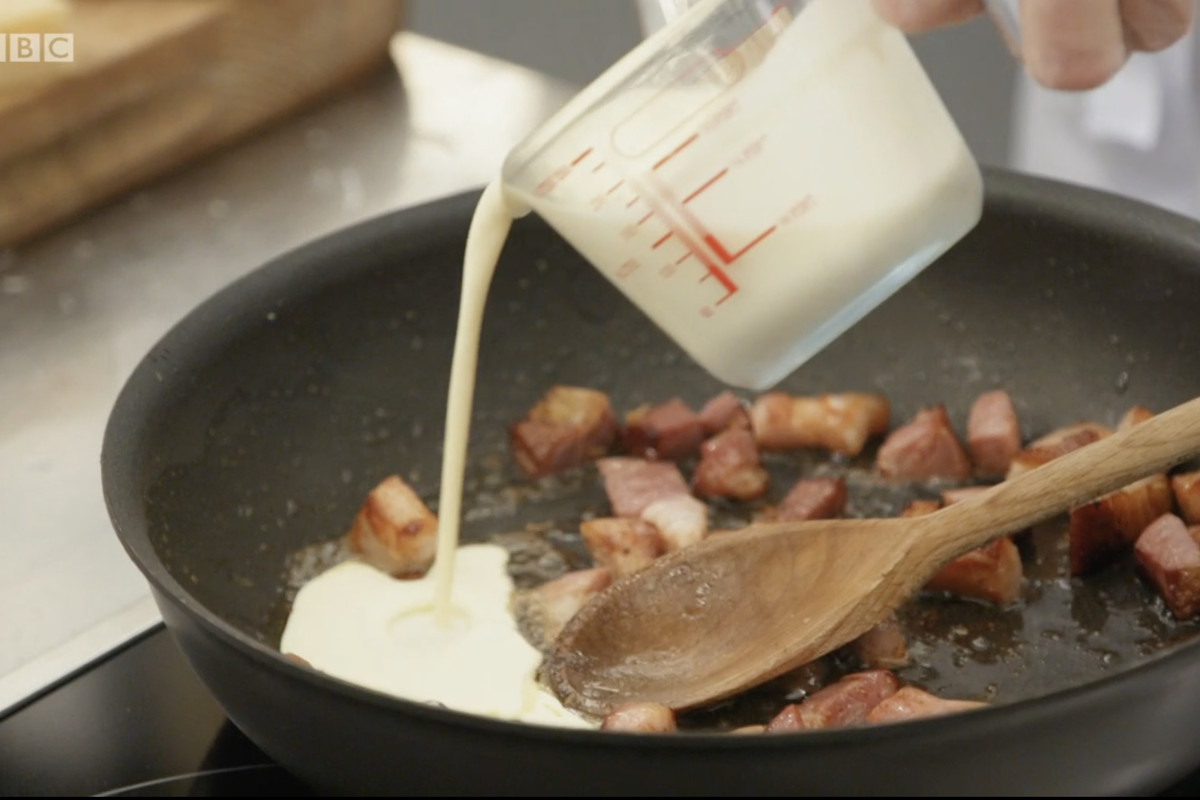 A Pyrex jug of cream being poured into a frying pan of sizzling smoked bacon, to make an entirely incorrect carbonara sauce